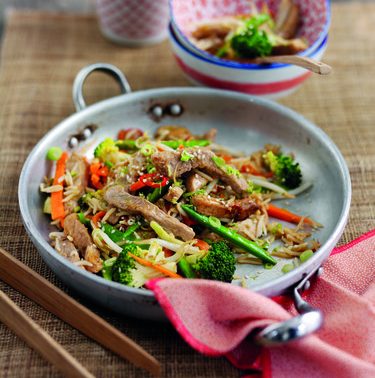 A delicious oriental-style pork stir-fry served in a pan, accompanied by a bowl of rice and garnished with vibrant, colorful vegetables.